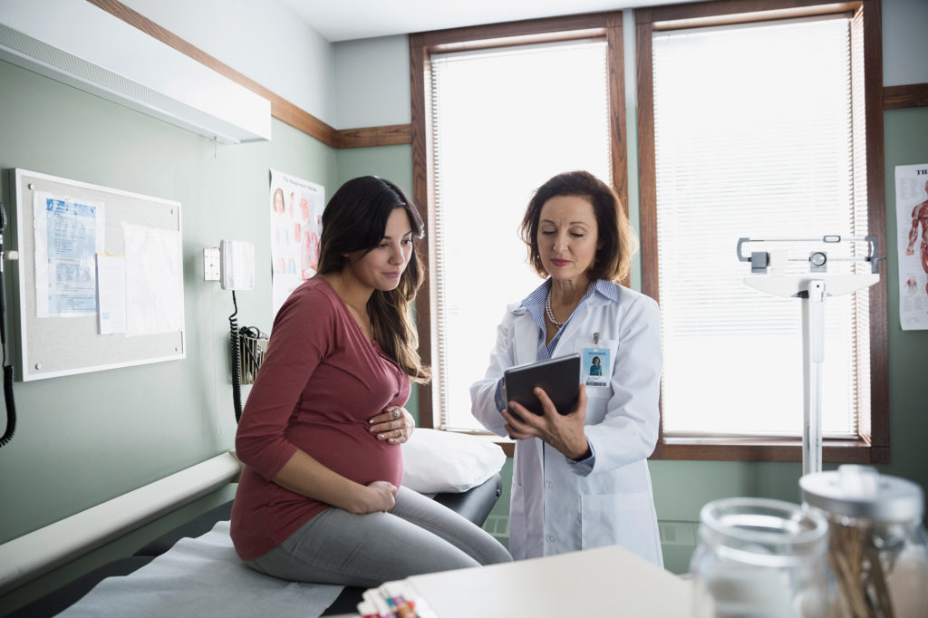 young pregnant woman looking at her results with her doctor on an iPad