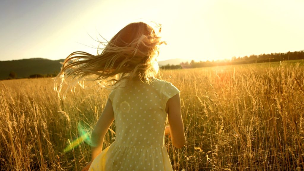 young girl running in a field towards sunset